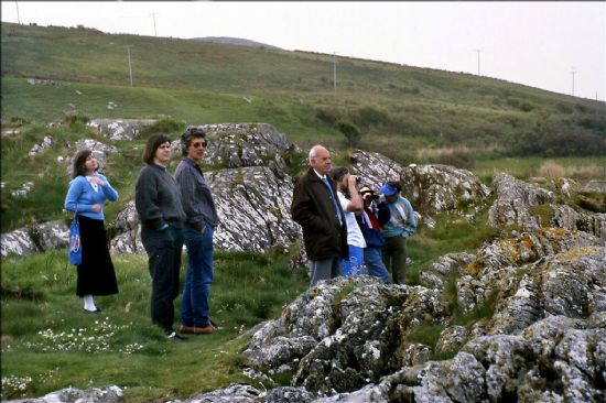 Group of people standing between rocks with grassy hillside behind them.