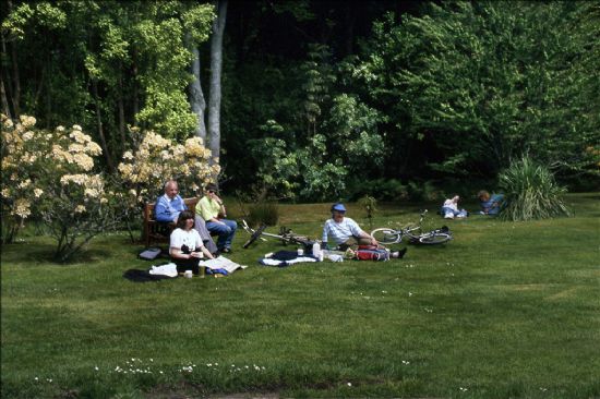 Group of people sitting on grass or benches in garden setting.