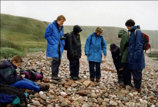 Group of people wearing waterproofs standing on a pebble beach
