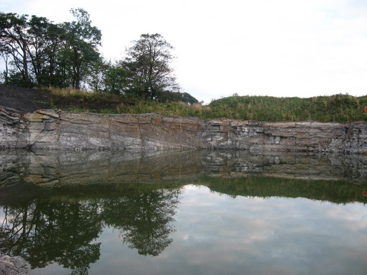 Large pond in quarry showing rockface and trees above.