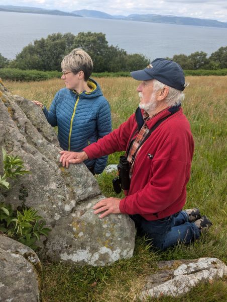 Two people kneeling next to a rock covered in lichens.