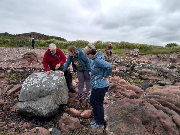 A group of people standing beside a large grey rock covered in pale lichens and surrounded by red sandstone rocks.