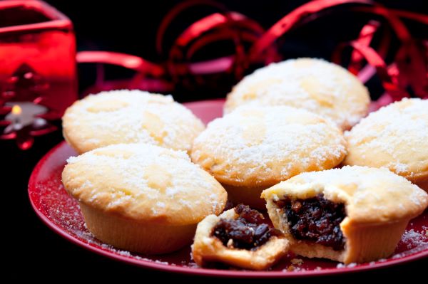 Close up of a plate containing 6 Christmas mince pies with one broken open showing the fruity filling.
