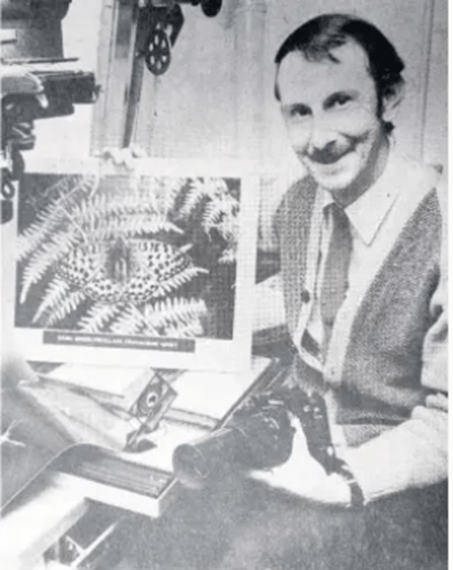 Black and white photograph of smiling Norman Tait holding a camera in one hand and prize-winning photograph in the other.