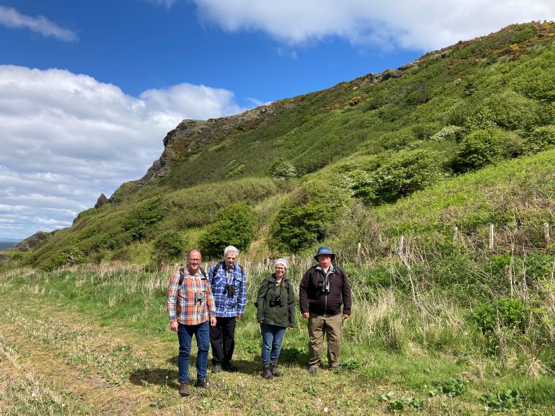group of 6 people standing in foreground with hill in the background