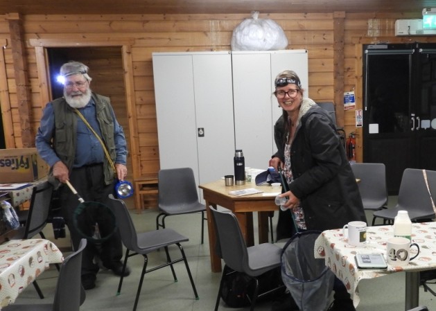 Two people holding moth nets in a room with tables and chairs