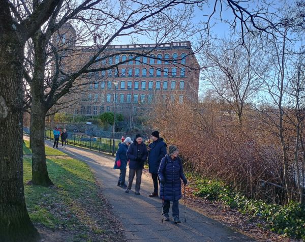 Groups of people on walkway between trees with large red brick building in background