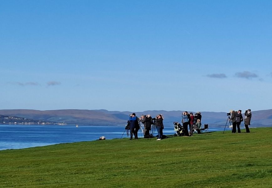 Group of people standing looking out to sea with binoculars and scopes on stands